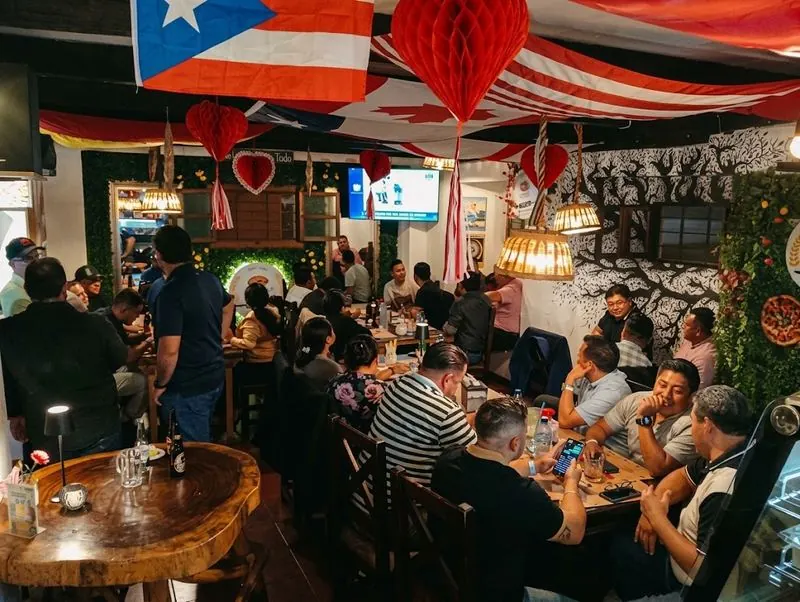Salón decorado con banderas y lámparas de mimbre, lleno de clientes